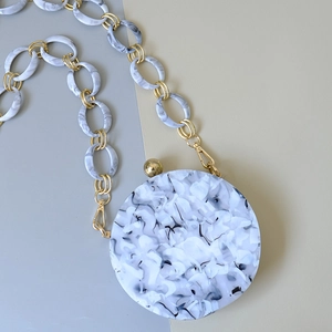 Detail of a marble textured round acrylic bag with chunky resin chain and gold metal hardware