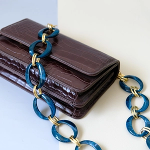 Detail of blue marble resin and gold metal chain strap on brown crocodile leather bag