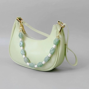 Detail of pistachio green half-moon bag featuring a decorative green and white resin chain