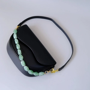 Detail of light green faceted bead chain on matte black saddle bag with gold hardware