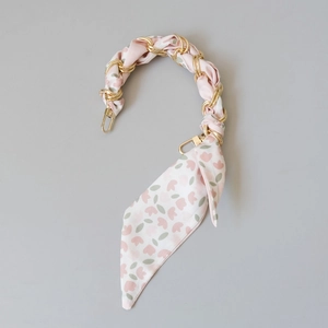 Détail d'une bandoulière en chaîne dorée enroulée d'un foulard en soie à fleurs