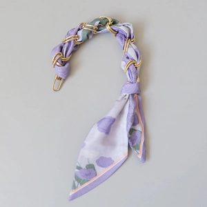 Détail d'un foulard en soie lilas tressé dans une chaîne de sac dorée élégante