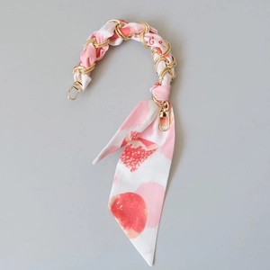Détail de la poignée en chaîne dorée entrelacée d'un foulard en soie rose pour sacs