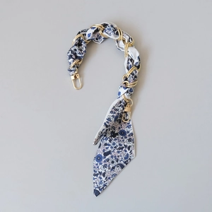 Détail de la poignée en soie à fleurs bleues entrelacée d'une chaîne en métal doré