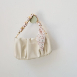 Détail d'une poignée en chaîne dorée enroulée d'un foulard en soie sur un sac crème