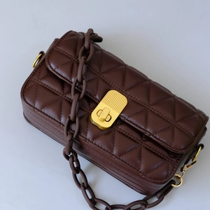 Close-up of dark brown quilted shoulder bag with gold hardware and chunky resin chain strap