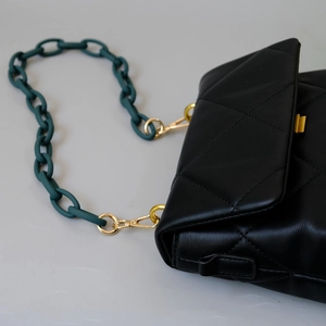 Detail of black quilted shoulder bag with matte dark green acrylic chain and gold lock
