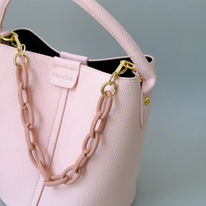 Close-up of pink lychee leather handbag with decorative resin chain and gold hardware