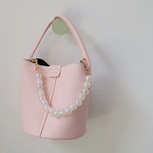 Pink lychee grain leather bucket bag featuring iridescent beaded handle on white wall