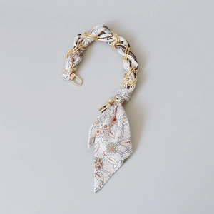 Detail of silk scarf intertwined with gold metal chain strap for handbags with lobster clasps