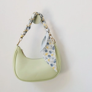 Detail of mint green crescent bag featuring golden metal chain wrapped with floral scarf