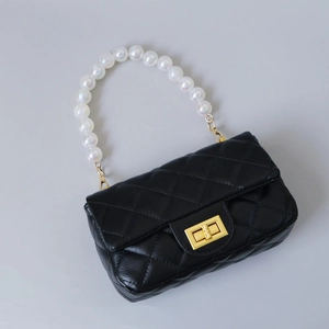 Close-up of black quilted handbag featuring large iridescent pearl handle and gold twist lock