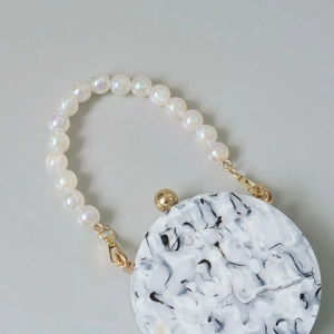Detail of round marble acrylic bag with iridescent pearl handle and gold metal clasp