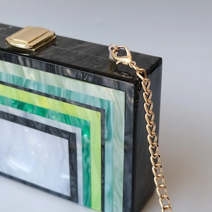Detailed macro view of green striped acrylic marble clutch with golden metal chain