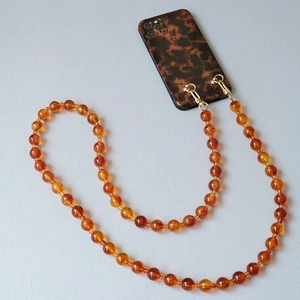 Detail of amber acrylic bead chain strap with golden metal spring clasps on phone case