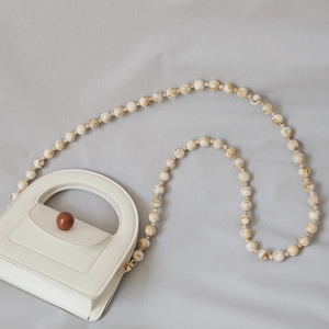 Detail of white mini bag with marble-textured bead strap and unique brown rotary lock