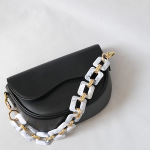 Black saddle bag with elegant marble acrylic and gold metal chain strap on grey background