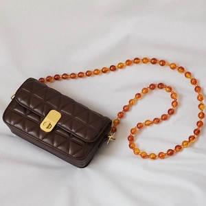 Detail of a brown quilted faux leather bag with an amber acrylic bead strap and gold lock
