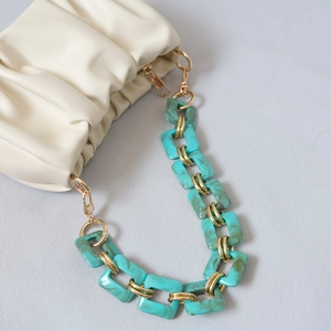 Macro detail of turquoise marble acrylic chain on off-white pleated leather bag