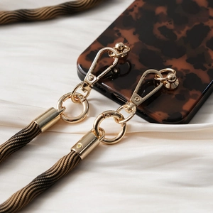 Detail of golden metal hooks and woven strap connected to tortoise pattern phone case