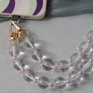 Detail of clear acrylic bead strap with pink accents and golden lobster clasp on phone case