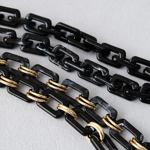 Detail view of black resin chain links with gold metal rings for handbag accessories