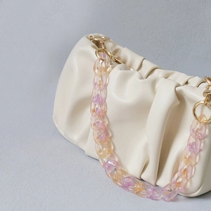Détail d'un sac à main plissé blanc cassé avec une chaîne décorative en acrylique dégradé