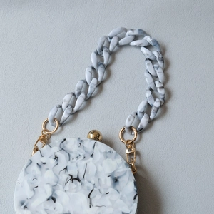 Detailed close-up of marble pattern acrylic handbag with chunky chain and gold metal clasp