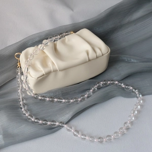 Beige pleated cloud clutch bag featuring a transparent acrylic bead chain strap on blue fabric