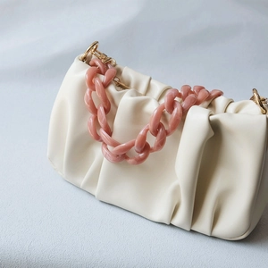 Close-up of pink acrylic chain strap on beige dumpling bag with gold metal hooks
