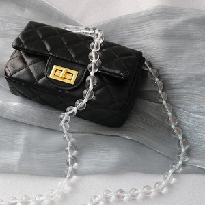 Detail of black quilted mini bag with transparent acrylic bead chain and gold lock