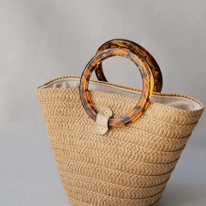 Detail of hand-woven straw bag with tortoiseshell resin handle and cream leather closure