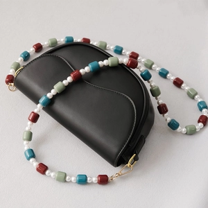 Detail of black saddle bag featuring colorful resin beads and pearl crossbody strap