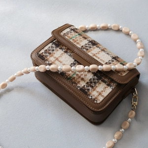 Detail of tweed crossbody bag with brown leather trim and unique beaded pearl shoulder strap