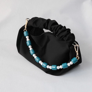 Detail of black pleated handbag featuring blue resin beads and white pearl strap accents