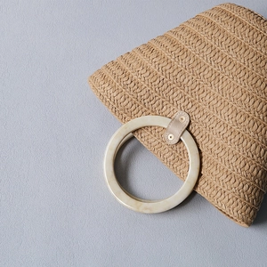 Close-up of a marbled resin handle and woven straw texture on a vintage tote bag