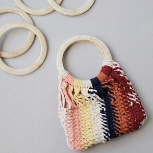 Detail showing colorful woven texture and marble-patterned resin handle of the handbag