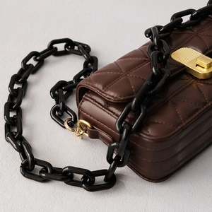 Détail d'un sac matelassé marron foncé avec chaîne en résine noire et fermoir doré chic