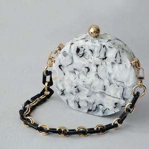 Macro shot of marble-textured acrylic clutch bag with golden metal spherical clasp