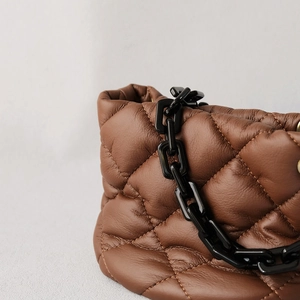 Detail of dark brown quilted leather bag with thick black chain strap and pleated design