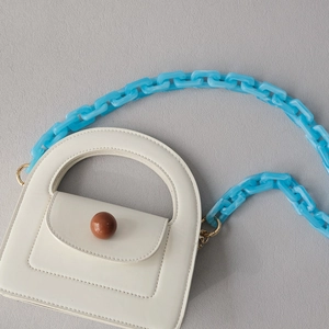Mini off-white handbag featuring a bold blue acrylic chain strap and brown sphere clasp