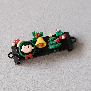 Detail showing a black phone clip with 3D resin Christmas boy, bell, tree and candy cane motifs