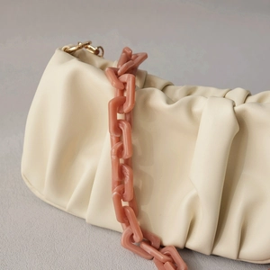 Close-up of cream pleated pouch bag featuring a chunky pink acrylic resin chain strap