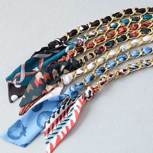 Detail of silk scarf intertwined with gold metal chains and lobster clasps for handbags