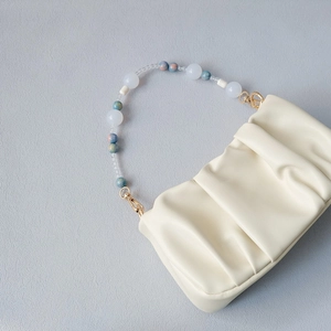Detail of creamy pleated handbag with luxury handcrafted beaded handle and gold hardware