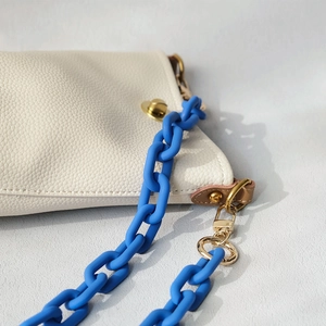 Close-up of bright blue chunky resin chain on a beige grained leather handbag detail