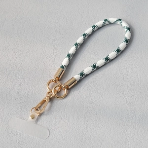 Détail de la dragonne de téléphone tressée vert et blanc avec fermoir en métal doré et pad