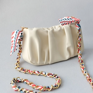 Detail of creamy white cloud bag with golden chain strap entwined with a colorful silk scarf
