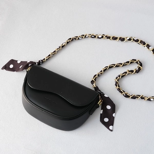 Detail of black leather handbag featuring a gold chain strap woven with polka dot silk scarf