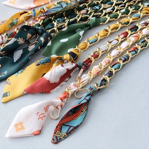 Detail of golden metal chain straps interwoven with silk scarves for designer handbags
